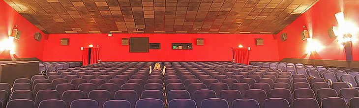 Panoramabild: Dieses Foto eines Kinos beschert uns einen fast surrealen Eindruck. Der Betrachters schaut frontal und direkt in die Zuschauerplätze hinein. Farben und Konturen sind überzeichnet scharf. Das Licht von den Seitenwänden strahlt wie Scheinwerfer.